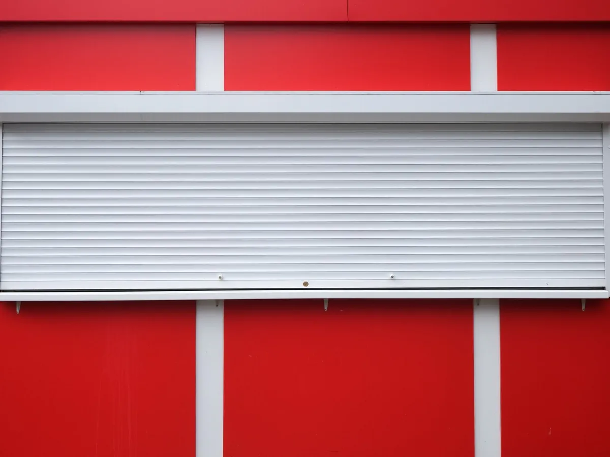 Volet roulant à lames blanches baissé sur le guichet d'un kiosque à façade rouge